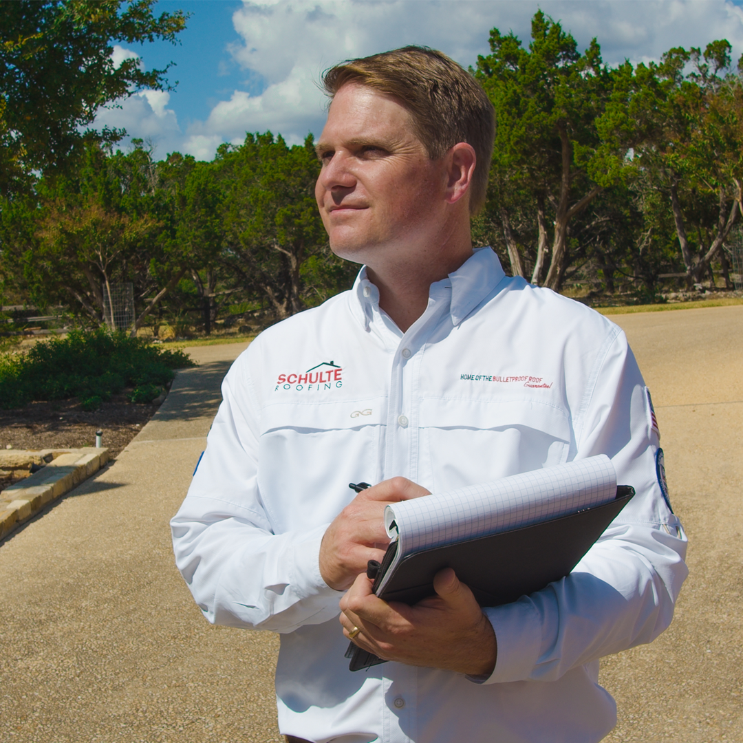 A Schulte Roofing Project Manager in a crisp white long sleeve shirt with the Schulte Roofing logo on the above the shirt pocket.