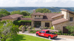 Residential home with handmade clay tile roof installed by Schulte Roofing, surrounded by lush greenery in Ingram, Texas.