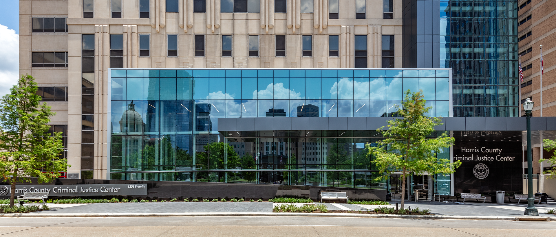 The Harris County Criminal Justice Center entryway from street view with the reflection of adjacent buildings in the window. Membrane roofing completed by Schulte Roofing.